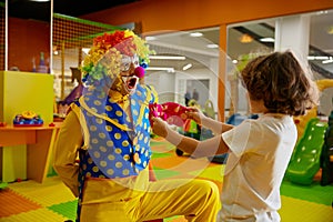 Funny clown animator and boy fooling around playing at indoor playroom