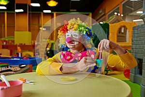 Funny clown playing with toy tea set at kids playroom