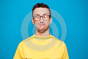 Funny comic man in glasses makes grimace with crosses eyes. Young man in yellow t-shirt with crazy expression has fun alone