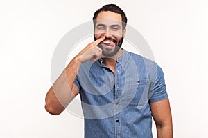 Funny comical man with beard picking finger to nose and showing tongue, looking at camera with smile, having fun, fooling around,
