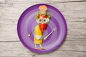 Funny cook with fork made of vegetables on plate