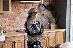 Joyful millennial latina woman juggle with cherry tomatoes at kitchen