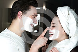 Funny couple handsome man applying jokingly foam on beautiful woman`s nose having fun both with shaving foam on their