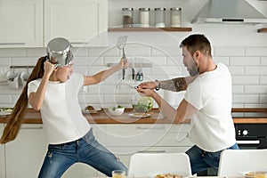 Funny couple having fun fighting with kitchen utensils cooking t
