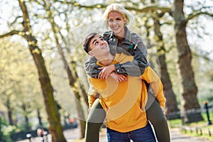 Funny couple in a urban park. Boyfriend carrying his girlfriend on piggyback.