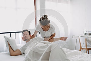 Funny couple wife try to wake lazy husband up in white bedroom.