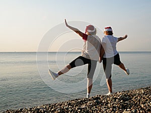 Funny Couple of women in santa claus hats on the sea beach, silhouette women as Santa hats hold hands and raise arms and legs. two