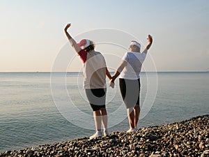 Funny Couple of women in santa claus hats on the sea beach, silhouette women as Santa hats hold hands and raise arms a. two drunk