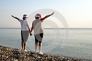 Funny Couple of women in santa claus hats on the sea beach, silhouette women as Santa hats hold hands and raise arms a. two drunk