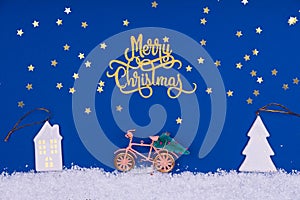 Funny cozy scene with Christmas toys on classic blue. Christmas tree is moved home by bicycle on the snow road with