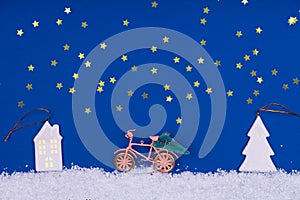 Funny cozy scene with Christmas toys on classic blue. Christmas tree is moved home by bicycle on the snow road with