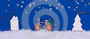 Funny cozy scene with Christmas toys on classic blue. Christmas tree is moved home by bicycle on the snow road with