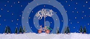 Funny cozy scene with Christmas toys on classic blue. Christmas tree is moved home by bicycle on the snow road with