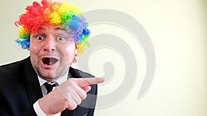 Funny crazy businessman with colored wig he is having fun and pointing his finger to the side.
