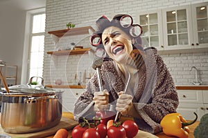 Funny crazy cheerful woman standing in kitchen and holding kitchenware