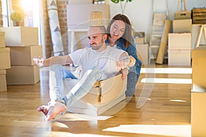 Funny and crazy couple having fun riding a cardboad box as a car, smiling happy and laughing at new home