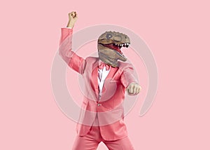 Funny crazy man in pink suit and dinosaur mask dancing isolated on pink background