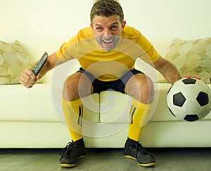 Funny and crazy soccer fan man dressed in his team uniform watching football game on television celebrating scoring goal excited