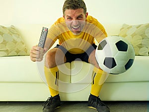 Funny and crazy soccer fan man dressed in his team uniform watching football game on television celebrating scoring goal excited