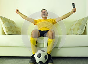 Funny and crazy soccer fan man dressed in his team uniform watching football game on television celebrating scoring goal excited