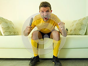 Funny and crazy soccer fan man dressed in his team uniform watching football game on television celebrating scoring goal excited