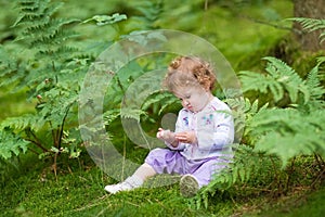 Funny curly baby girl eating wild raspberries in forest