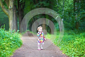 Funny curly baby girl in rain boots walking in a park