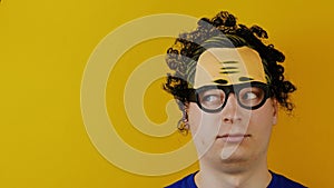 Funny curly guy turns or rolls his eyes, crazy cheerfully human emotions, on yellow wall background, black hairs