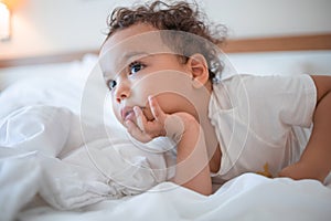 Funny curly toddler lying on the bed and attentively watching TV