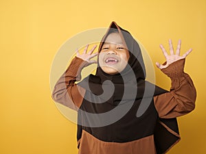 Funny cute Asian muslim little girl wearing hijab looked happy and laughing, against yellow