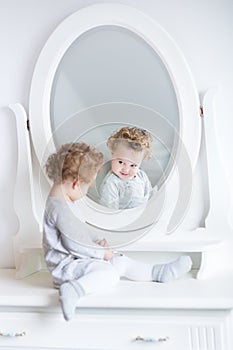 Funny cute baby girl watching her reflection in a white bedroom