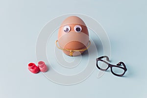 A funny cute brown egg with black glasses and red shoes on blue background