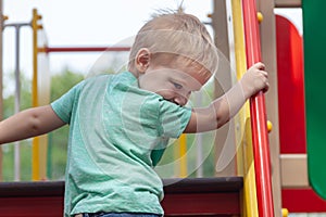 Funny cute caucasian blonde baby boy plays on the playground, climbing to upstair.