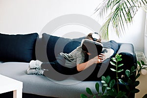 Funny cute girl watching something that is displayed in goggles of virtual reality, lying on the couch