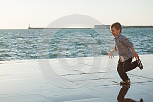 Funny cute little boy running along the sea coast in the city