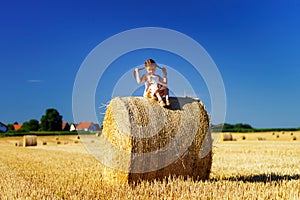 Funny cute little girl posing on the haystack in summer field