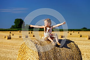 Funny cute little girl posing on the haystack in summer field