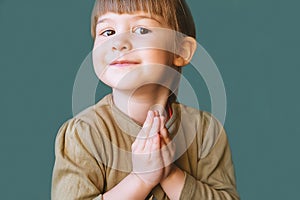 Funny Cute little girl praying on a blue background with a place to copy. The blonde, happy, smiling little girl folded her hands