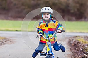 Funny cute preschool kid boy in safety helmet and colorful raincoat riding his first bike