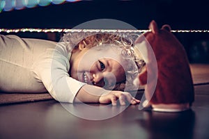 Funny cute smiling baby playing hide and seek under the bed with toy hamster in vintage style