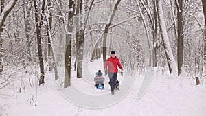 Funny dad carries two children in a sled on a winter alley.