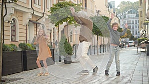 Funny dance of cheerful grandfather and grandchildren on sunny city street. Wide shot portrait of joyful senior man