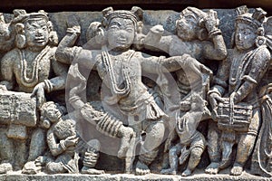 Funny dancing people in traditional Indian clothes. Relief of 12th century Hindu temple Hoysaleshwara in Halebidu, India