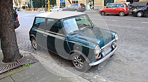 Funny dark green small old little italian mini car with round headlights and green bright body and white top on roman street