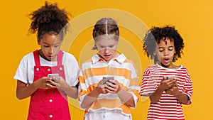 Funny delighted multinational kids use smartphone on yellow background