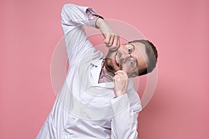 Funny doctor makes a smile by holding mouth with hands, he does not lose heart and entertains patients. Pink background.