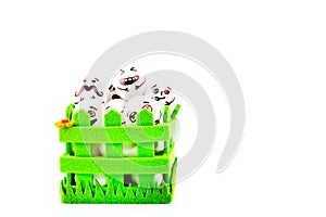 Funny easter eggs with different funny faces in the green basket on white.