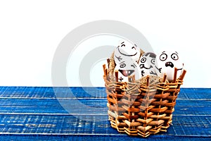 Funny easter eggs with different funny faces in the basket on white and blue.