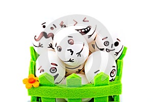 Funny easter eggs with different funny faces in the green basket on white background.