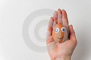 Funny egg with face lies on female hand on white background. Food with Funny Faces